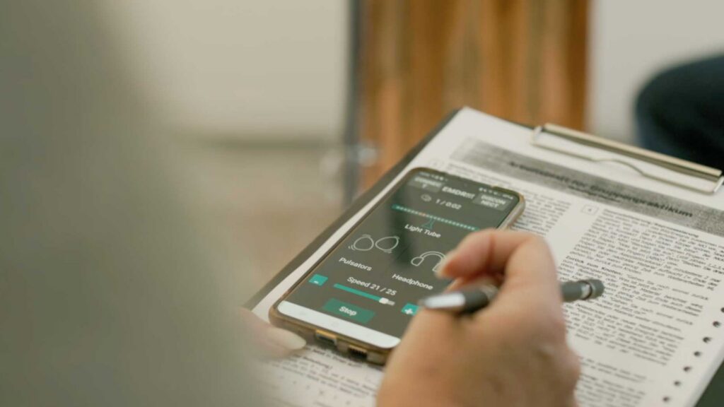 Szene aus dem ZDF-Beitrag: Eine Therapeutin hält ein Smartphone mit einer EMDR-App über einem Arbeitsblatt.